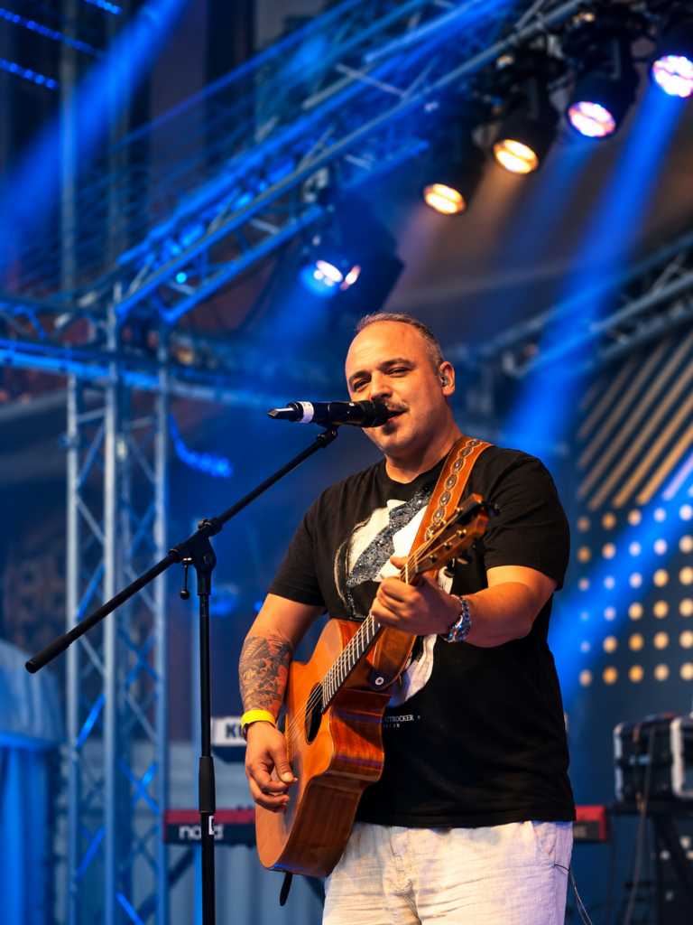 Dagobert Weiß singt mit Akustikgitarre auf der Bühne